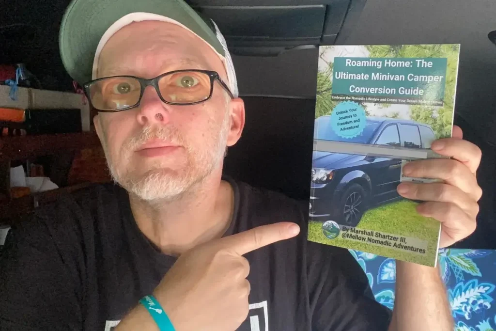 Marshall Shartzer III holding the Roaming Home minivan camper conversion guide inside Voyager